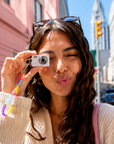 Woman holding mini digital camera with beaded lanyard wristlet outdoors