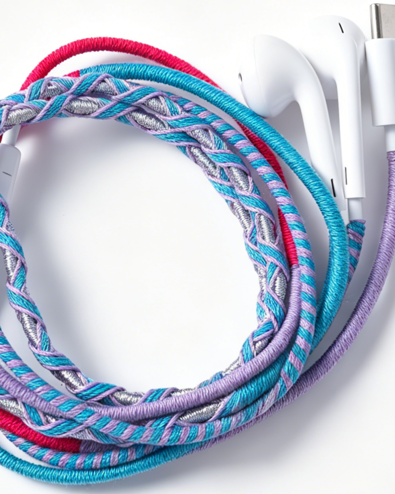 Braided wired earphones with a colorful twisted cable in turquoise, purple, pink, and silver, shown with white earphone tips on a white background.