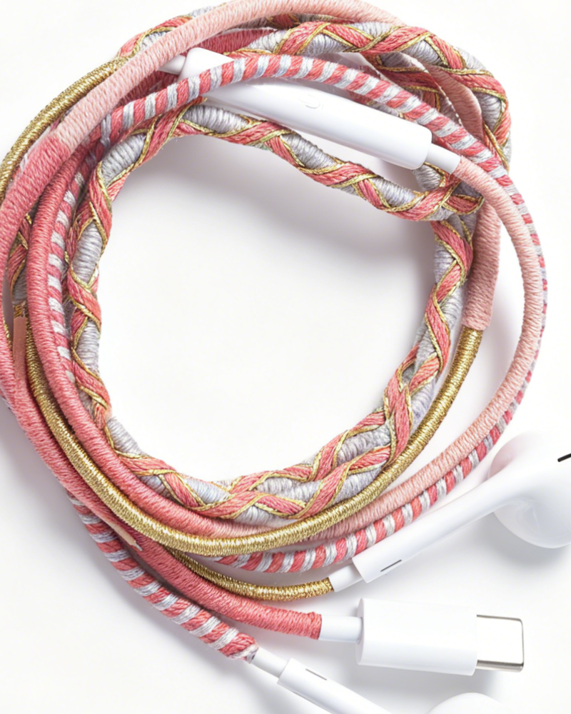 A braided headphone cable with pink, white, and metallic gold threads, featuring white inline controls and USB-C connectors, photographed on a clean white background.