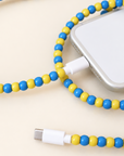 Blue and yellow USB-C beaded cable connected to an iPhone on cream background