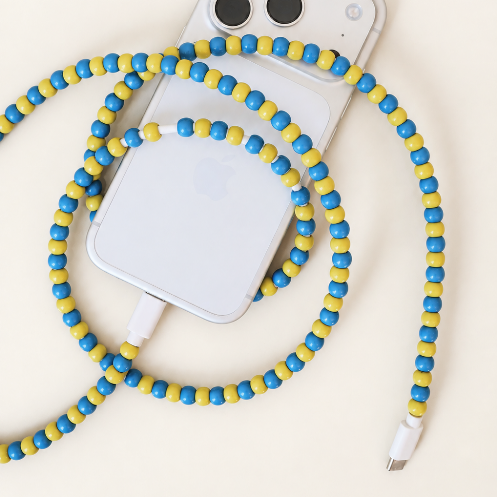 Blue and yellow USB-C beaded cable looped around an iPhone on cream background