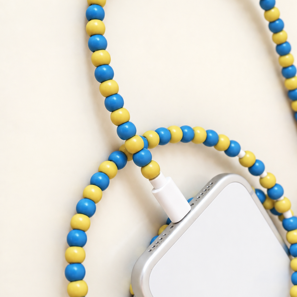 Blue and yellow USB-C beaded cable looped around an iPhone on cream background