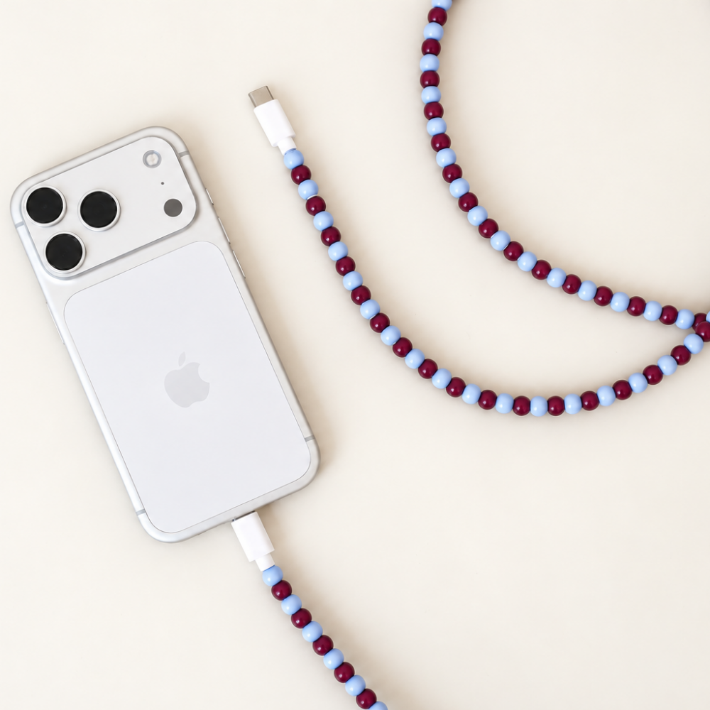 Burgundy and light blue USB-C beaded cable connected to a silver iPhone on cream background