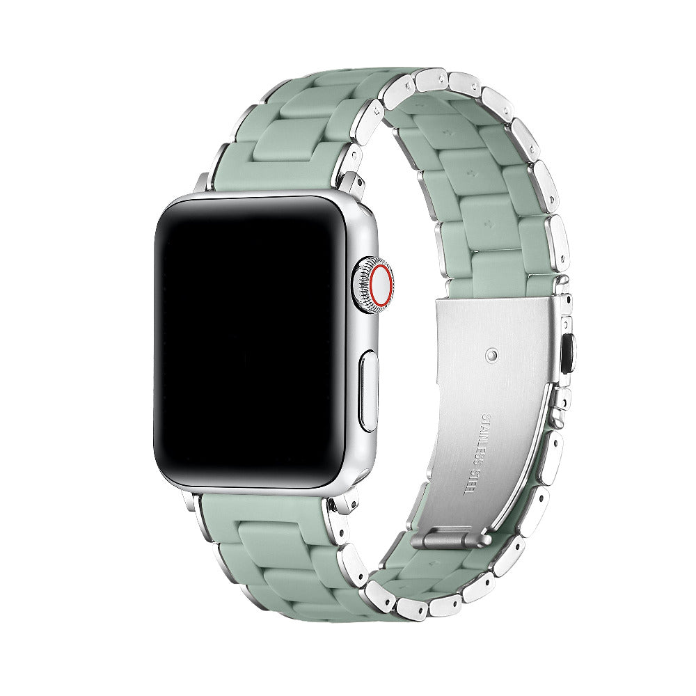 A silver smartwatch with a light sage green link band, shown on a clean white background. The band has a polished metallic finish with a matte green center on each link.