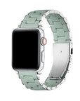 A silver smartwatch with a light sage green link band, shown on a clean white background. The band has a polished metallic finish with a matte green center on each link.