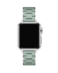 A silver smartwatch with a rectangular black screen and a light sage green metal link band, shown against a plain white background.