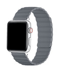 A silver smartwatch with a rectangular black screen and a gray wavy silicone band, shown on a plain white background.